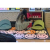 Person in a classroom setting with colorful chairs and a smiley face rug.