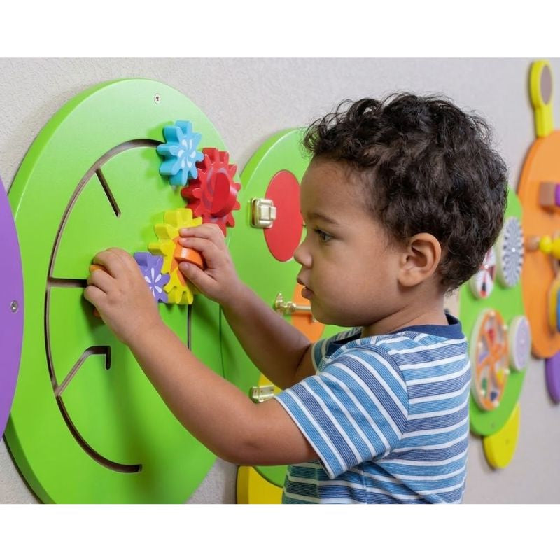 Child playing with a colorful educational wall panel featuring gears.