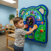 Child interacting with a colorful educational wall panel in a room with chairs and a table.