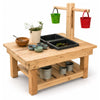 A wooden toy garden playset with a sandbox, small planters, hanging buckets in green and red, and storage bins on a white background.