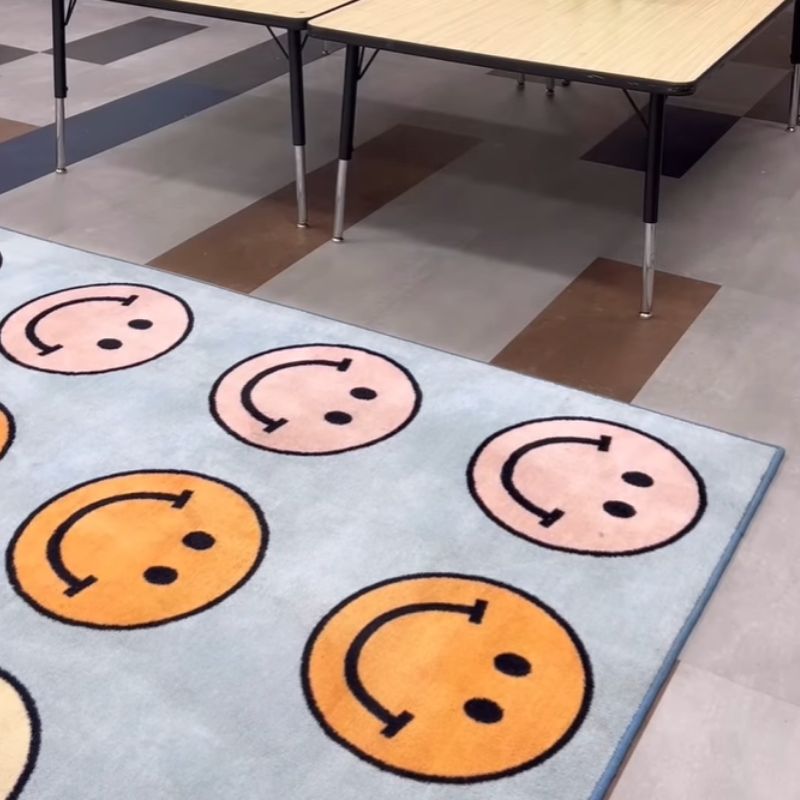 Colorful smiley face rug on a checkered floor with tables in the background