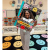 Person holding a decorative frame with smiley faces on a SensoryEdge classroom rug