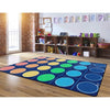 A colorful children's play rug with a grid pattern of large colored circles on a dark blue background, shown on a wooden floor in a playroom setting.
