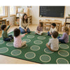 Children sitting on a green rug with a teacher in a classroom setting.