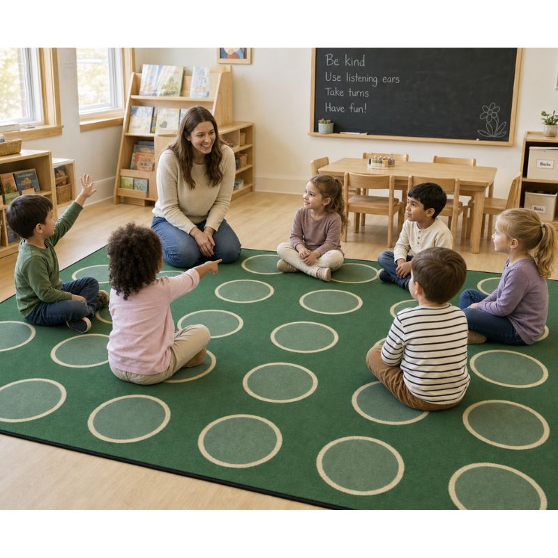 Children sitting on a green rug with a teacher in a classroom setting.