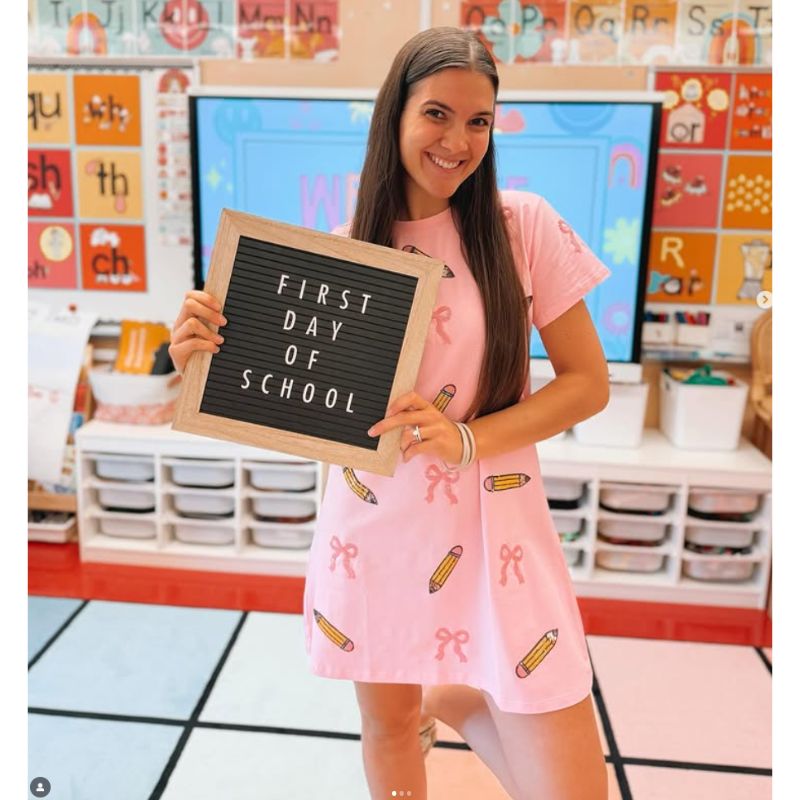 Teacher holding a 'First Day of School' sign ion a classroom rug