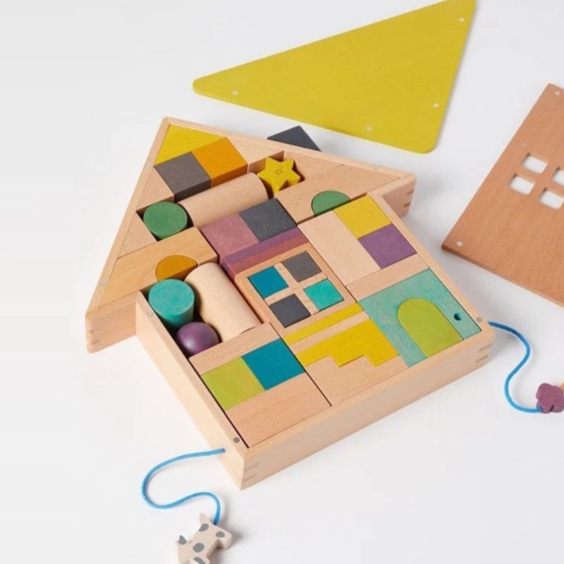 A wooden house-shaped toy block set with colorful geometric shapes and small hanging animal charms, photographed on a clean white background.