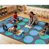 Children and a teacher playing on a large mat with colorful circles in a classroom setting. Twilight Tides Seating Rug by SensoryEdge.