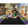 Two children sitting on a colorful classroom rug in a library with bookshelves in the background.