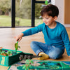 Child playing with a toy dinosaur and small animal on a wooden floor.