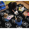 Children sitting on a black rug with white floral patterns, reading books.