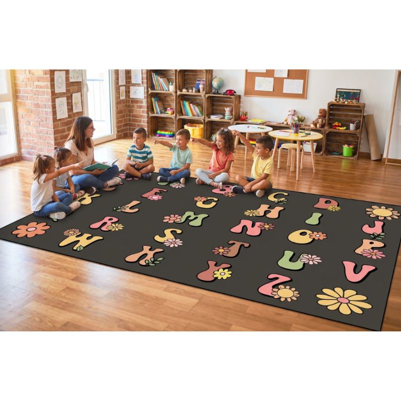 Children and a teacher sitting on a colorful alphabet and flower carpet in a busy classroom.