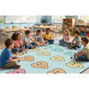 Children sitting on a colorful rug with smiley face patterns in a classroom setting.
