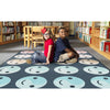 Two children sitting on the happy harmony rug with smiley face patterns in a library setting.

