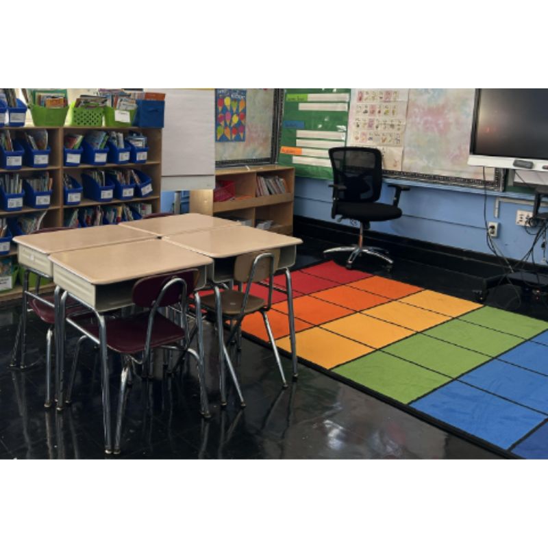 Classroom with colorful rug, desks, and chairs.