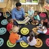 Teacher reading to children on a rug with smiley face patterns in a classroom setting.