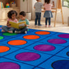 Children reading a book on a colorful floor mat in a classroom setting.
